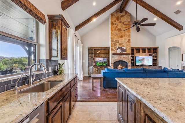 7817 Bella Flora Dr, Fort Worth, TX 76126 - kitchen with visible vents, light stone countertops, beamed ceiling, a stone fireplace, and a ceiling fan