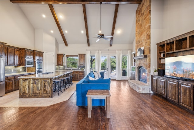 living room featuring ceiling fan, high vaulted ceiling, wood-type flooring, and a stone fireplace