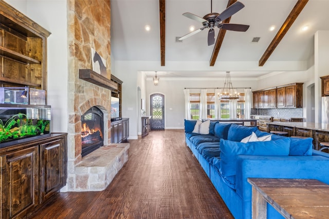 living room with beam ceiling, dark wood-type flooring, a stone fireplace, and ceiling fan with notable chandelier