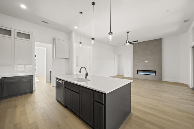 kitchen featuring a fireplace, ceiling fan, a kitchen island with sink, sink, and white cabinets