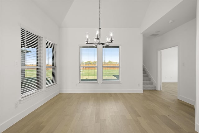 unfurnished dining area with light hardwood / wood-style floors, vaulted ceiling, and a notable chandelier