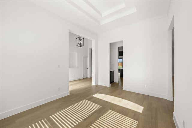 spare room with a raised ceiling, crown molding, a chandelier, and light wood-type flooring