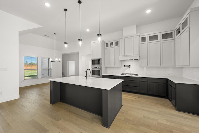 kitchen featuring white cabinetry, light hardwood / wood-style flooring, an island with sink, decorative light fixtures, and appliances with stainless steel finishes