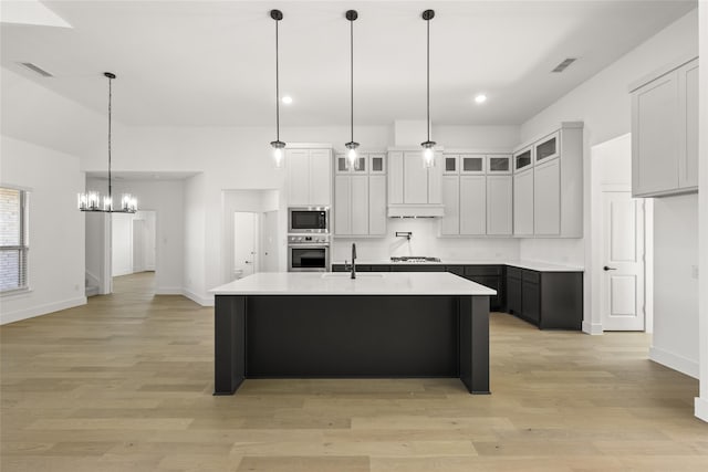 kitchen with a center island with sink, hanging light fixtures, appliances with stainless steel finishes, light hardwood / wood-style floors, and white cabinetry