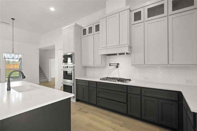 kitchen with pendant lighting, white cabinets, sink, light hardwood / wood-style flooring, and appliances with stainless steel finishes