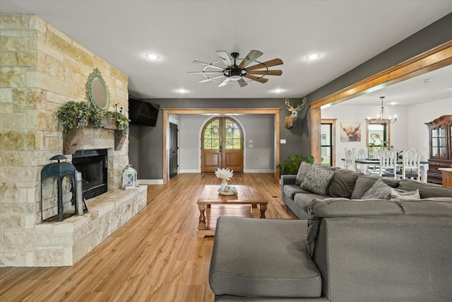 living room with a stone fireplace, ceiling fan with notable chandelier, and light wood-type flooring