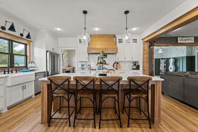 kitchen featuring custom range hood, white cabinetry, and an island with sink