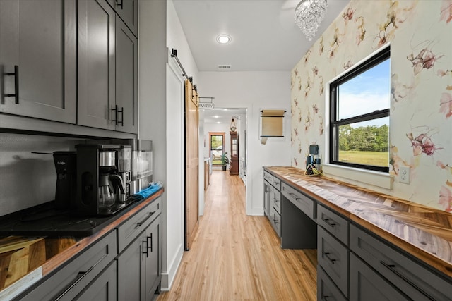 kitchen featuring gray cabinetry, light hardwood / wood-style floors, wood counters, and a barn door