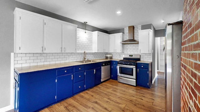 kitchen with white cabinets, appliances with stainless steel finishes, light hardwood / wood-style floors, wall chimney exhaust hood, and sink