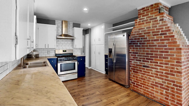 kitchen featuring wall chimney range hood, white cabinetry, blue cabinetry, appliances with stainless steel finishes, and dark hardwood / wood-style flooring