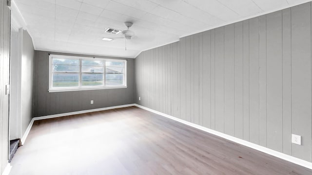 empty room featuring hardwood / wood-style floors, ceiling fan, and wood walls