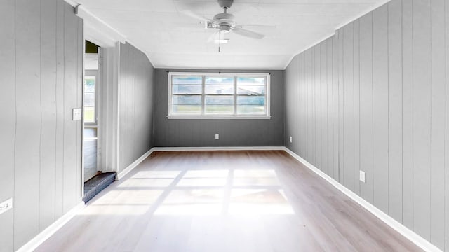 empty room featuring lofted ceiling, wooden walls, wood-type flooring, and ceiling fan