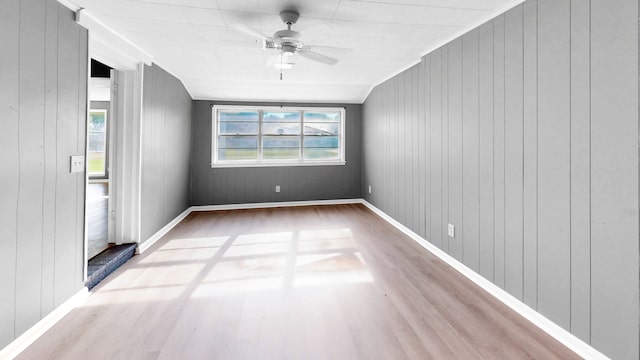 empty room with ceiling fan, wood walls, and wood-type flooring