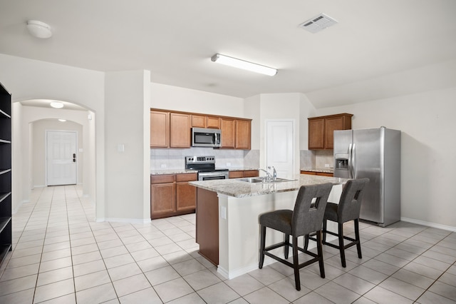 kitchen featuring backsplash, appliances with stainless steel finishes, a breakfast bar area, and a center island with sink