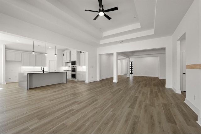 unfurnished living room with ceiling fan, hardwood / wood-style floors, a tray ceiling, and sink