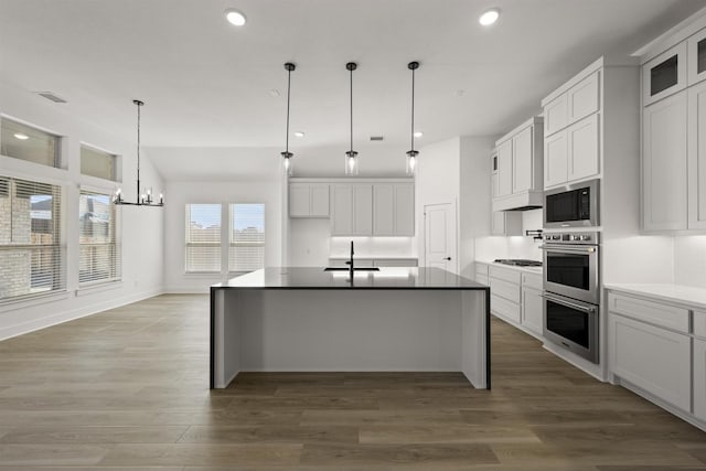 kitchen featuring white cabinets, appliances with stainless steel finishes, decorative light fixtures, a kitchen island with sink, and a notable chandelier