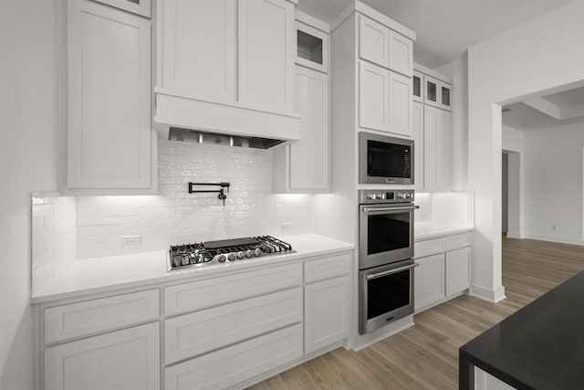 kitchen featuring tasteful backsplash, light wood-type flooring, appliances with stainless steel finishes, and white cabinetry