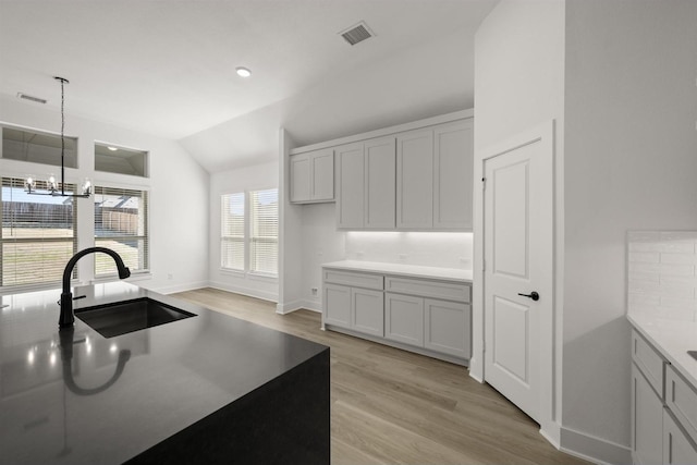 kitchen featuring decorative light fixtures, light wood-type flooring, lofted ceiling, a chandelier, and sink