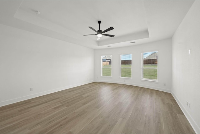 unfurnished room featuring ceiling fan, light hardwood / wood-style floors, and a tray ceiling