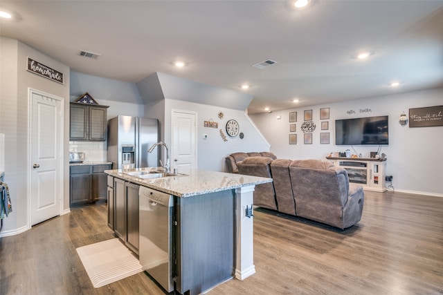 kitchen featuring a kitchen island with sink, sink, light stone countertops, appliances with stainless steel finishes, and wood-type flooring