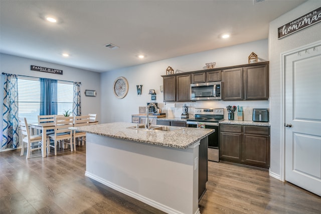 kitchen with dark wood-type flooring, stainless steel appliances, a center island with sink, and sink