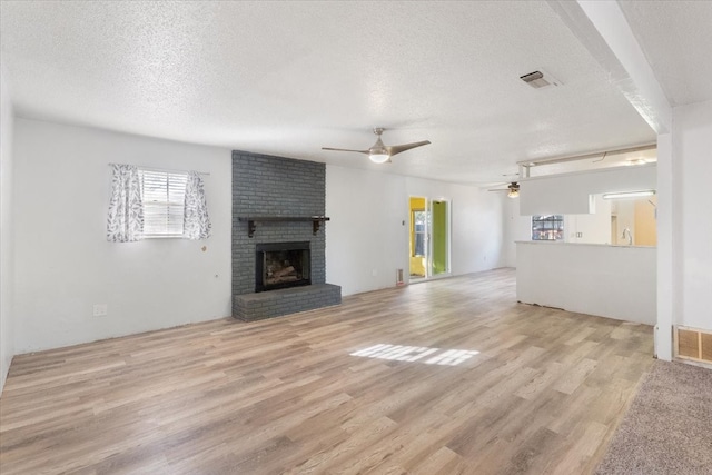 unfurnished living room featuring a textured ceiling, a fireplace, light wood-type flooring, and ceiling fan