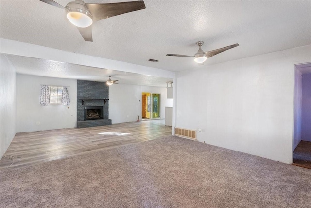 unfurnished living room featuring carpet flooring, a fireplace, a textured ceiling, a ceiling fan, and visible vents