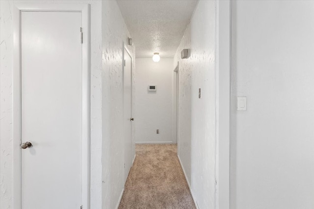 hallway with a textured ceiling and light colored carpet