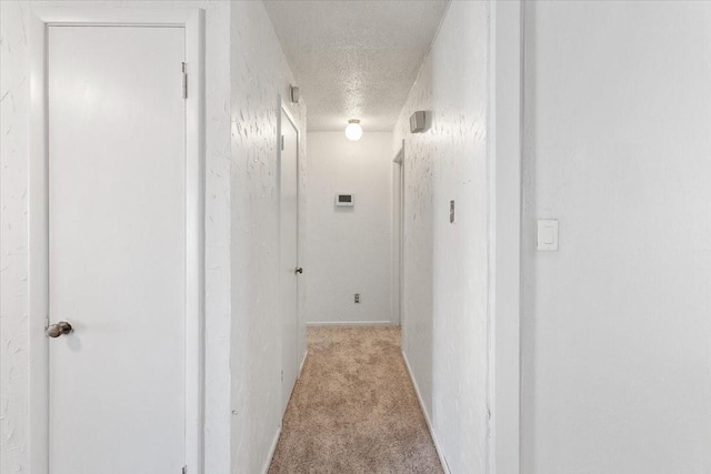 hallway featuring carpet floors, a textured ceiling, a textured wall, and baseboards