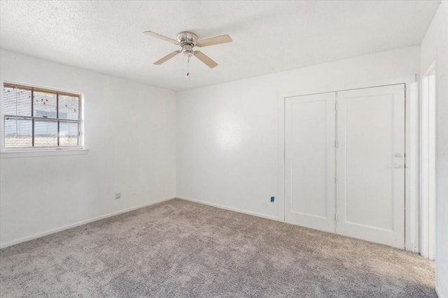 carpeted spare room featuring a textured ceiling, ceiling fan, and baseboards