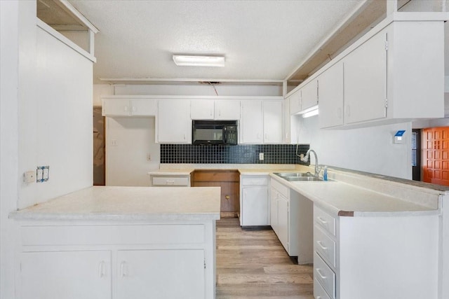 kitchen with black microwave, a sink, white cabinets, light wood finished floors, and a peninsula