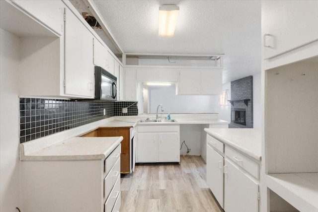kitchen with black microwave, a sink, light wood-style floors, white cabinetry, and tasteful backsplash