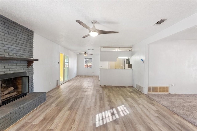 unfurnished living room featuring a ceiling fan, a brick fireplace, wood finished floors, and visible vents