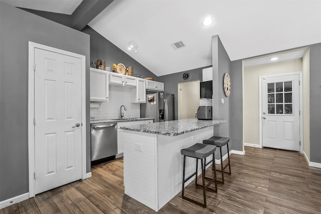 kitchen with vaulted ceiling with beams, a kitchen breakfast bar, stainless steel appliances, white cabinets, and dark hardwood / wood-style floors