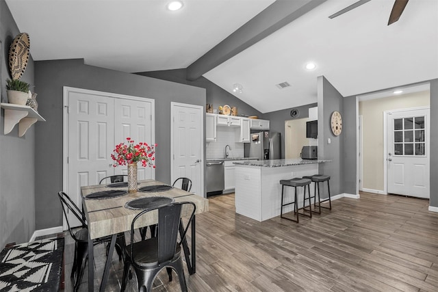 dining room featuring sink, lofted ceiling with beams, light hardwood / wood-style floors, and ceiling fan