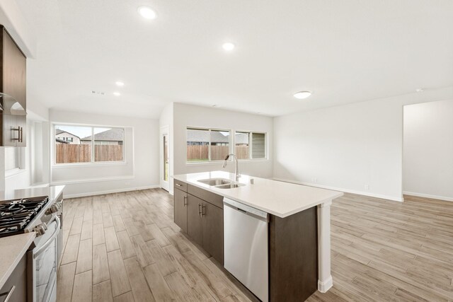 kitchen with dark brown cabinetry, sink, stainless steel appliances, light hardwood / wood-style flooring, and a kitchen island with sink