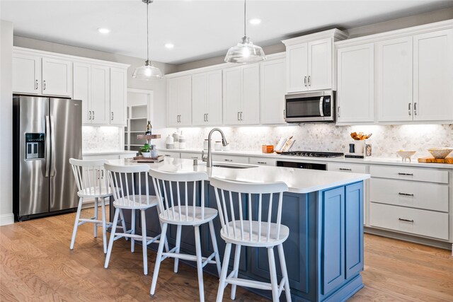 kitchen with stainless steel appliances, a center island with sink, sink, light wood-type flooring, and pendant lighting