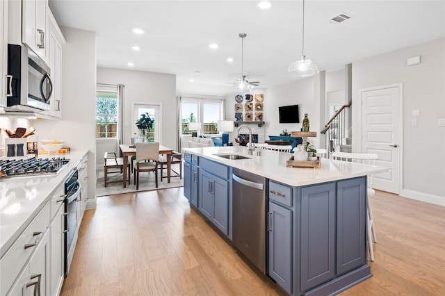 kitchen with sink, stainless steel appliances, an island with sink, white cabinets, and decorative light fixtures