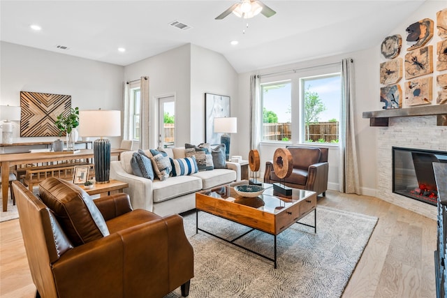 living room with plenty of natural light, a fireplace, vaulted ceiling, and light hardwood / wood-style flooring