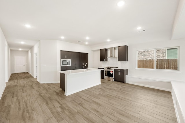 kitchen with a wealth of natural light, light hardwood / wood-style flooring, stainless steel gas range oven, and wall chimney range hood