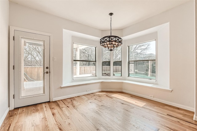 unfurnished dining area with a wealth of natural light, a notable chandelier, and light hardwood / wood-style floors