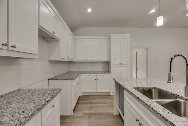 kitchen featuring sink, light wood-type flooring, hanging light fixtures, vaulted ceiling, and white cabinets