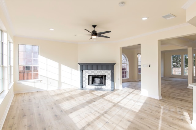 unfurnished living room featuring ceiling fan, a stone fireplace, ornamental molding, and light wood-type flooring