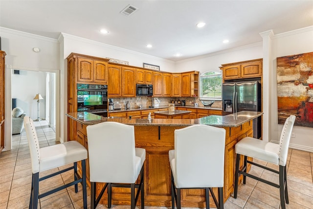 kitchen featuring crown molding, a kitchen island with sink, a breakfast bar, and black appliances