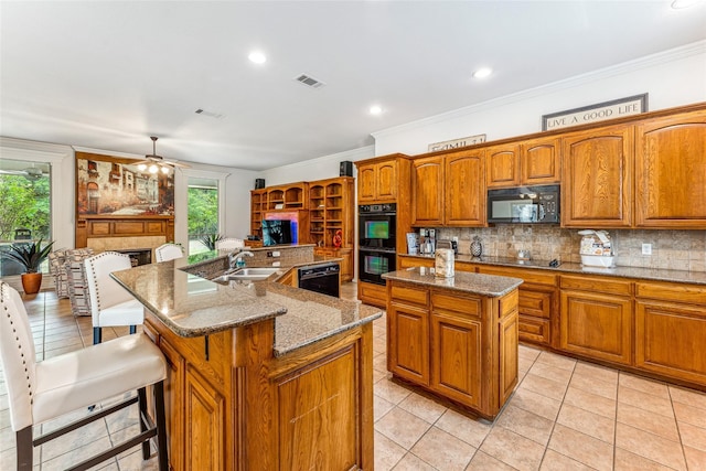 kitchen featuring black appliances, backsplash, light tile patterned floors, and an island with sink