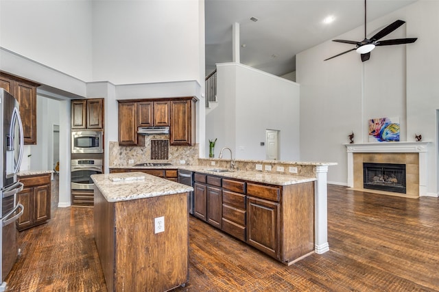 kitchen featuring sink, light stone counters, appliances with stainless steel finishes, a kitchen island, and a fireplace