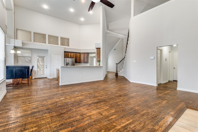 unfurnished living room with a high ceiling, dark hardwood / wood-style floors, and ceiling fan with notable chandelier