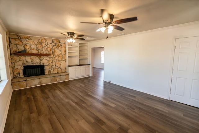 unfurnished living room featuring ceiling fan, dark wood-type flooring, a stone fireplace, built in features, and crown molding