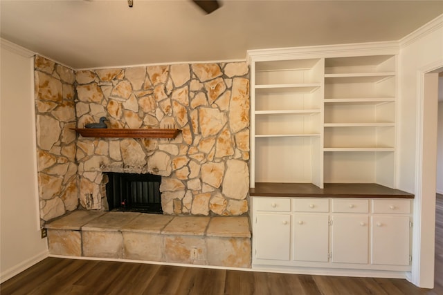 unfurnished living room featuring dark hardwood / wood-style flooring, a stone fireplace, and crown molding