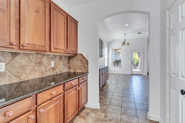 kitchen with decorative backsplash, light tile patterned floors, an inviting chandelier, vaulted ceiling, and dark stone countertops